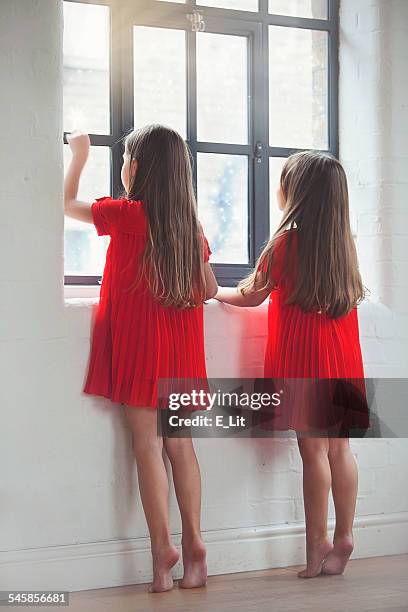 girls (4-5) in red dresses looking out through window - girl looking through window stock pictures, royalty-free photos & images