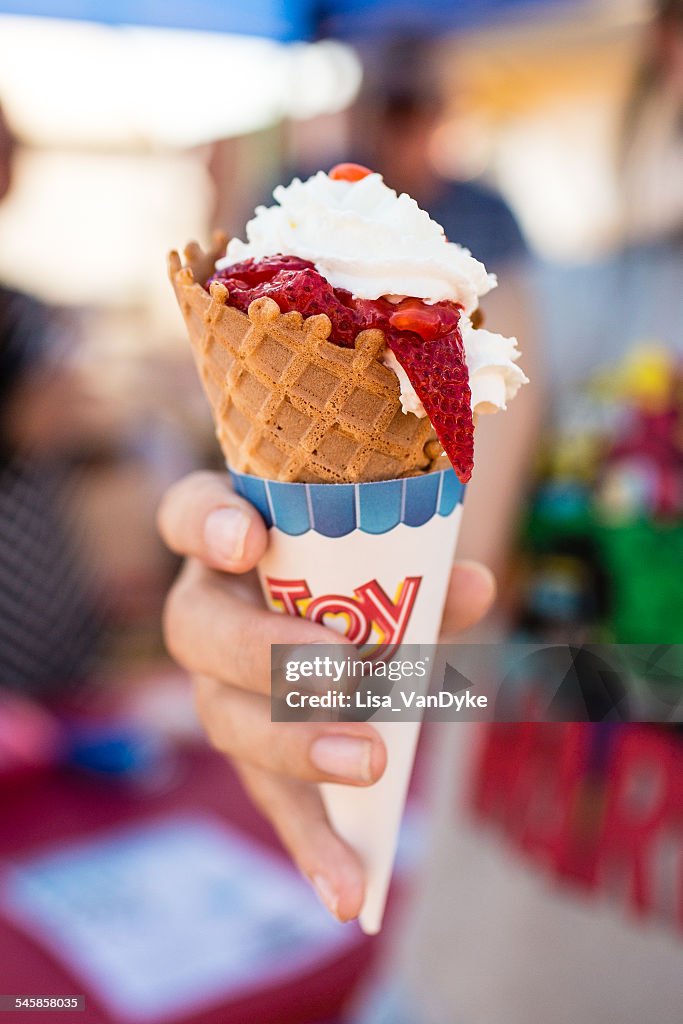 Young woman's hand holding ice cream cone with strawberries