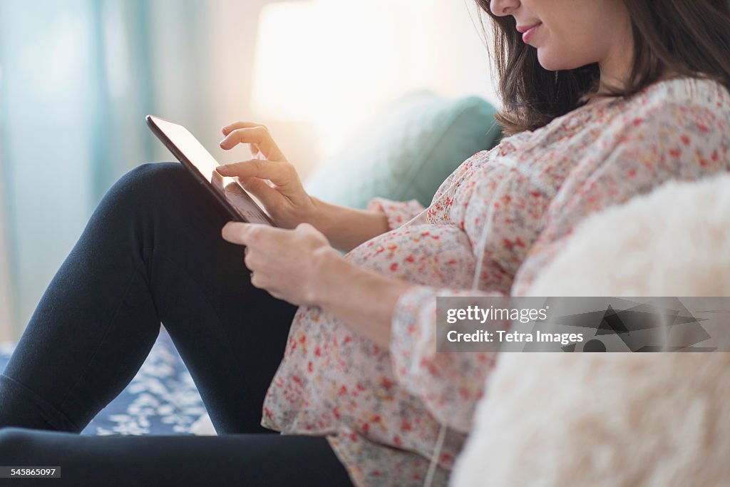 USA, New Jersey, Pregnant woman sitting on bed using tablet