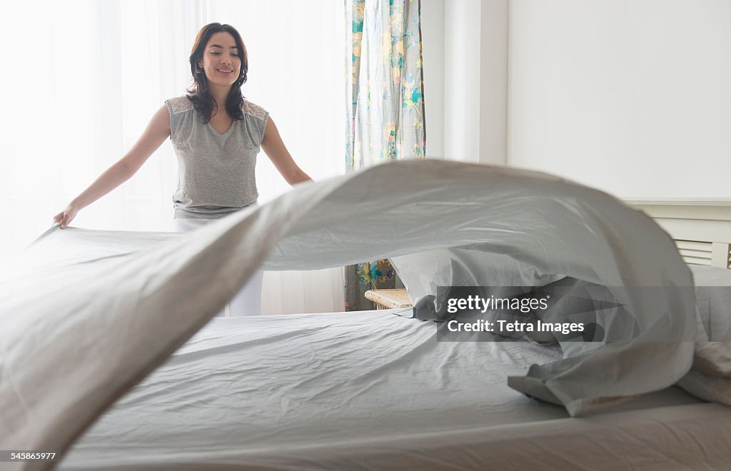USA, New Jersey, Young woman spreading sheet on bed