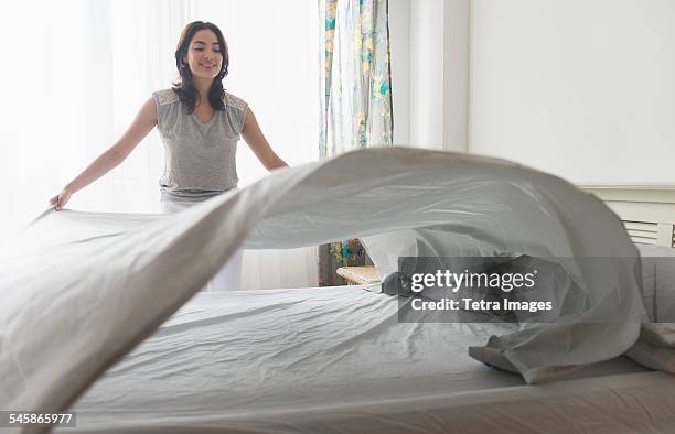 usa, new jersey, young woman spreading sheet on bed - bedsheets stockfoto's en -beelden