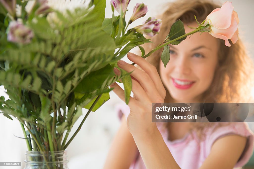 USA, New Jersey, Smiling young woman putting flowers in vase