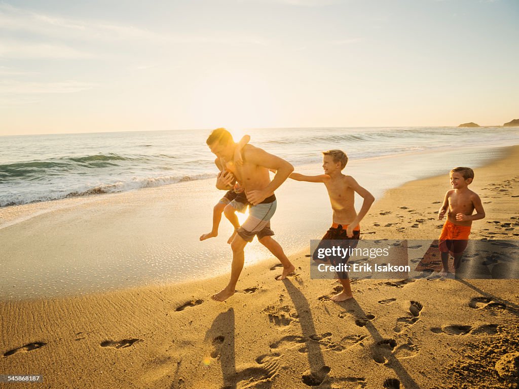 USA, California, Laguna Beach, Father playing football on beach with his three sons (6-7, 10-11, 14-15)