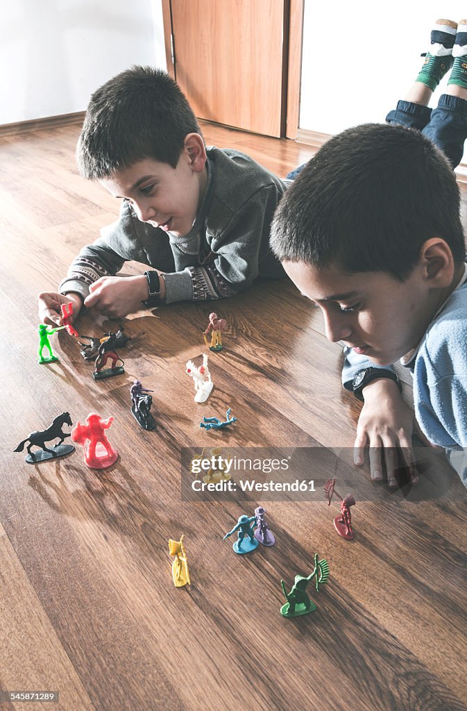 Two boys playing with miniature figurines on the floor at home