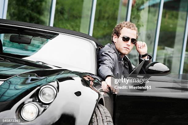 young man wearing sunglasses sitting in black sports car - símbolo de status imagens e fotografias de stock