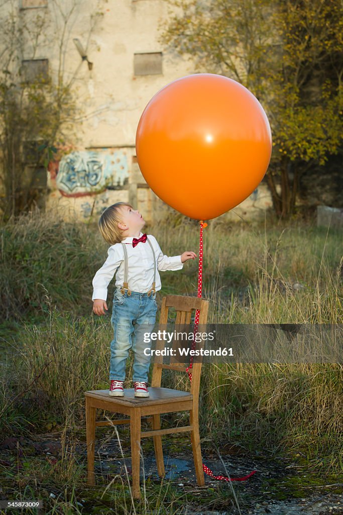 Boy standing on chair with balloon on meadow