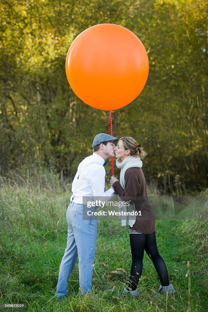 Couple with balloon on meadow kissing