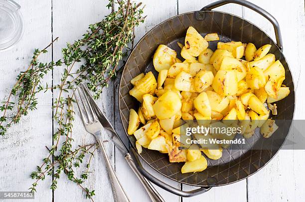 cast iron frying pan of fried potatoes, thyme and cutlery on wood - fried potato stock pictures, royalty-free photos & images