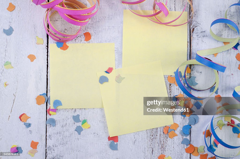 Three blank adhesive notes, confetti and streamers on wood