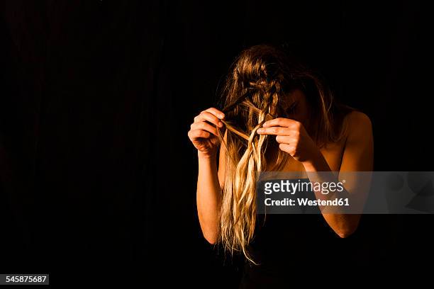 woman disentangling her hair in front of black background - frau haarsträhne blond beauty stock-fotos und bilder