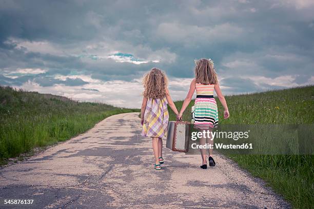 germany, bavaria, two girl walking on country road carrying old suitcase, rear view - bavaria girl stockfoto's en -beelden