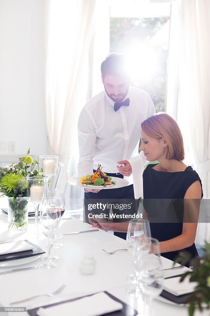 Waiter serving dinner to woman in elegant restaurant