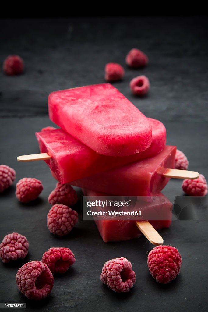 Raspberry ice lollies and frozen raspberries on black ground
