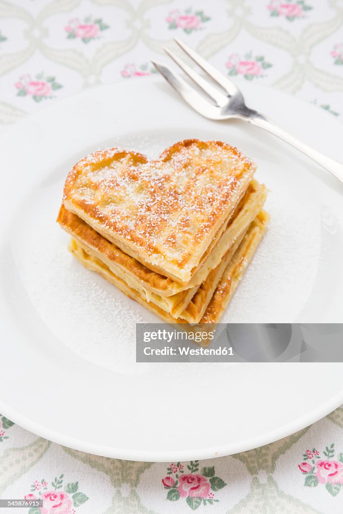 Dish of heart shaped waffles sprinkled with icing sugar on cloth