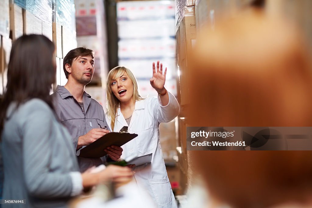 Woman in warehouse talking to worker with clipboard