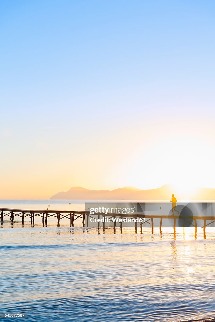 Spain, Balearic Islands, Majorca, man jogging on a jetty at sunrise
