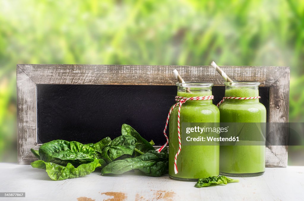 Two glasses of spinach smoothie, spinach leaves and blackboard