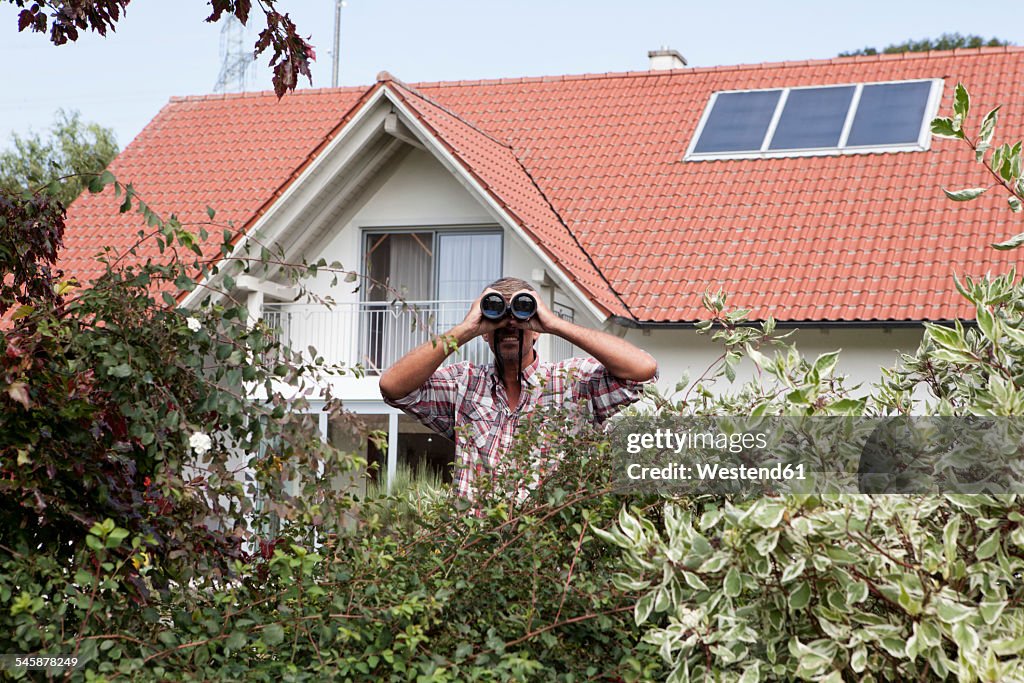 Man looking through binoculars over hedge