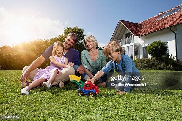happy family sitting on lawn in garden - stéréotype de la classe moyenne photos et images de collection