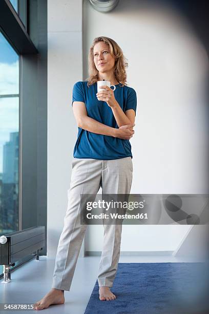 smiling mature woman with mug looking through window at her apartment - coffee cup top view fotografías e imágenes de stock