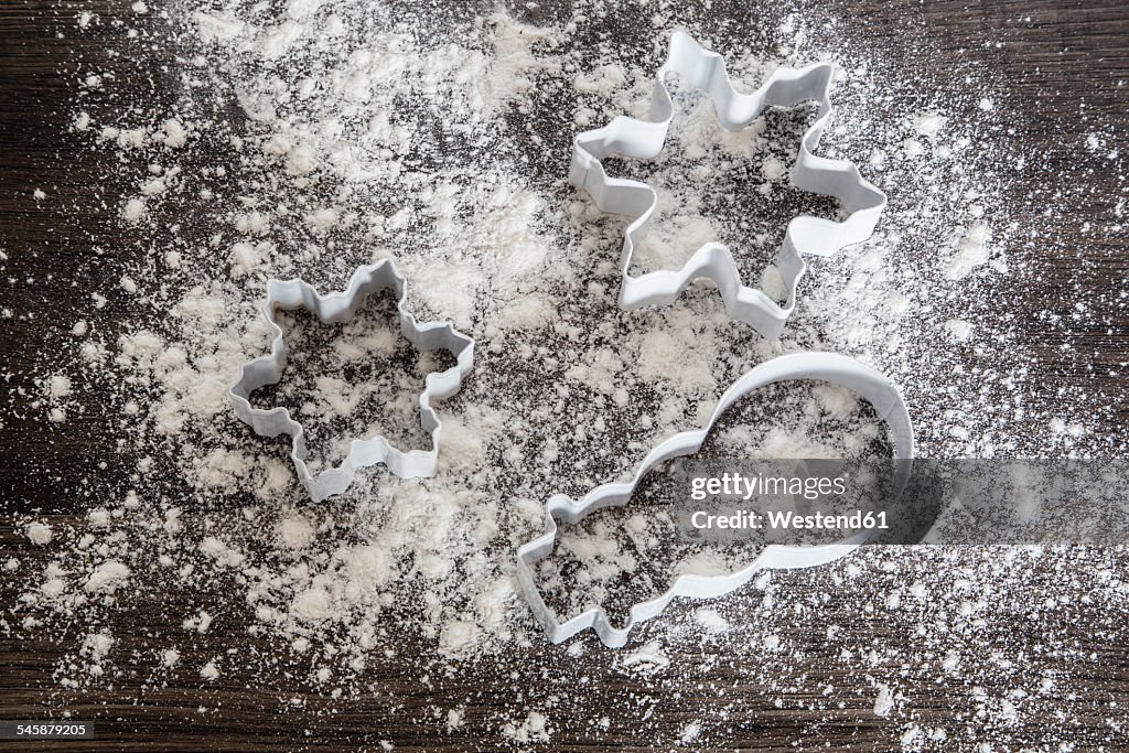 Three cookie cutters on scattered flour and dark wood