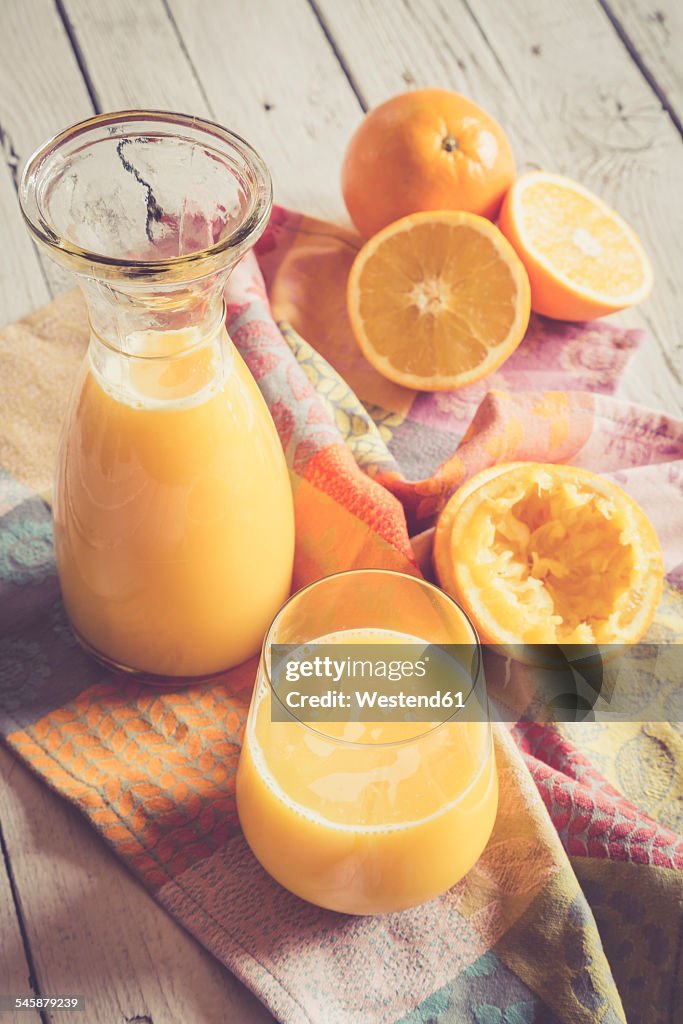 Oranges, carafe and glass of freshly squeezed orange juice on cloth and wood