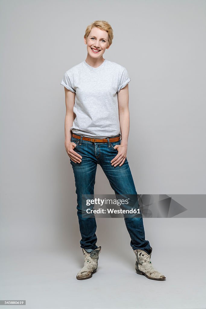 Relaxed woman with hands in her pockets standing in front of grey background