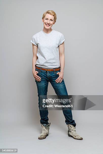 relaxed woman with hands in her pockets standing in front of grey background - tshirt jeans stockfoto's en -beelden