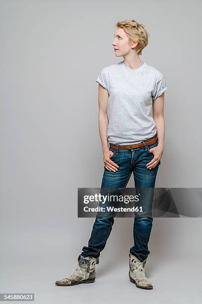 woman with hands in her pockets watching something in front of grey background - regard de côté studio photos et images de collection