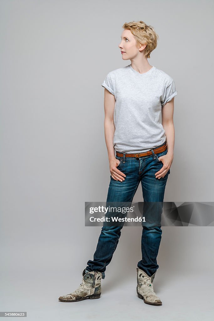 Woman with hands in her pockets watching something in front of grey background