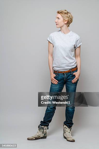 woman with hands in her pockets watching something in front of grey background - sideways glance stock pictures, royalty-free photos & images