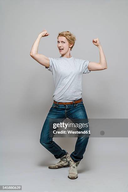 woman flexing her muscles in front of grey background - flexing muscles stockfoto's en -beelden