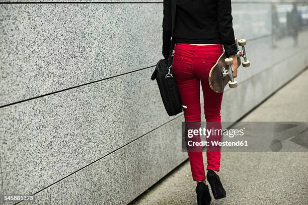 young woman with bag and skateboard wearing red trousers, partial view - business women pants stock-fotos und bilder