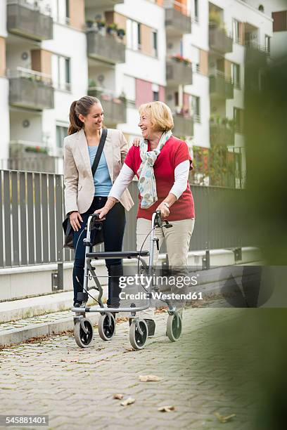 adult granddaughter assisting her grandmother walking with wheeled walker - oma rollator stockfoto's en -beelden