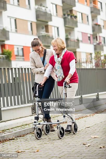 adult granddaughter assisting her grandmother walking with wheeled walker - oma rollator stockfoto's en -beelden
