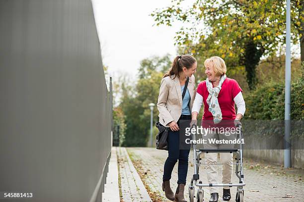 adult granddaughter assisting her grandmother walking with wheeled walker - senior young woman stockfoto's en -beelden