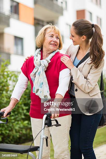 granddaughter assisting her grandmother walking with wheeled walker - oma rollator stockfoto's en -beelden