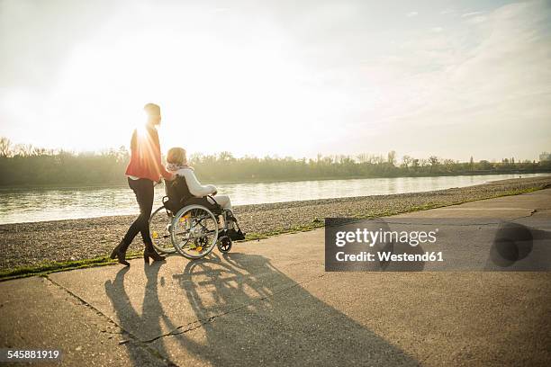 adult granddaughter assisting her grandmother sitting in wheelchair - pushing fotografías e imágenes de stock