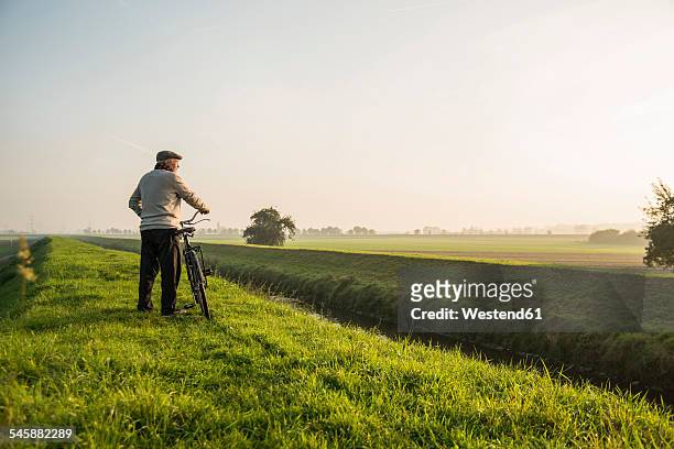 senior man in rural landscape pushing bicycle - meadow brook imagens e fotografias de stock