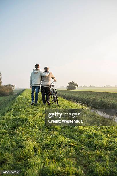 senior man and grandson in rural landscape with bicycle - dyke stockfoto's en -beelden