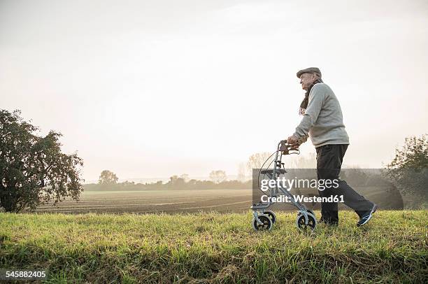 senior man with wheeled walker walking in rural landscape - looprek stockfoto's en -beelden