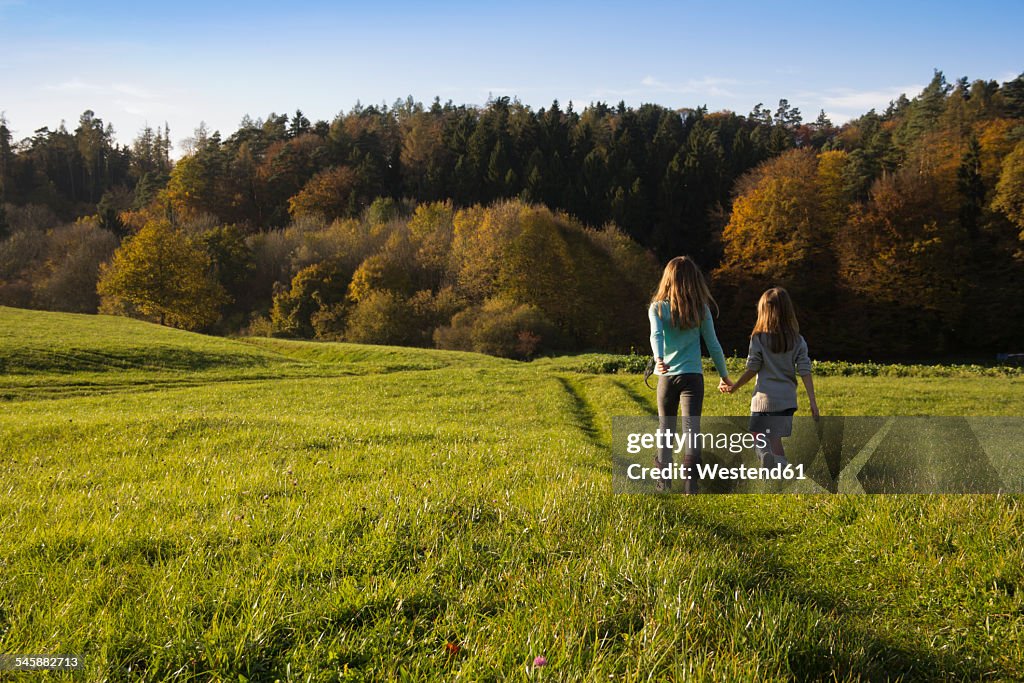 Germany, Bavaria, Landshut, two girls walking on meadow in autumn