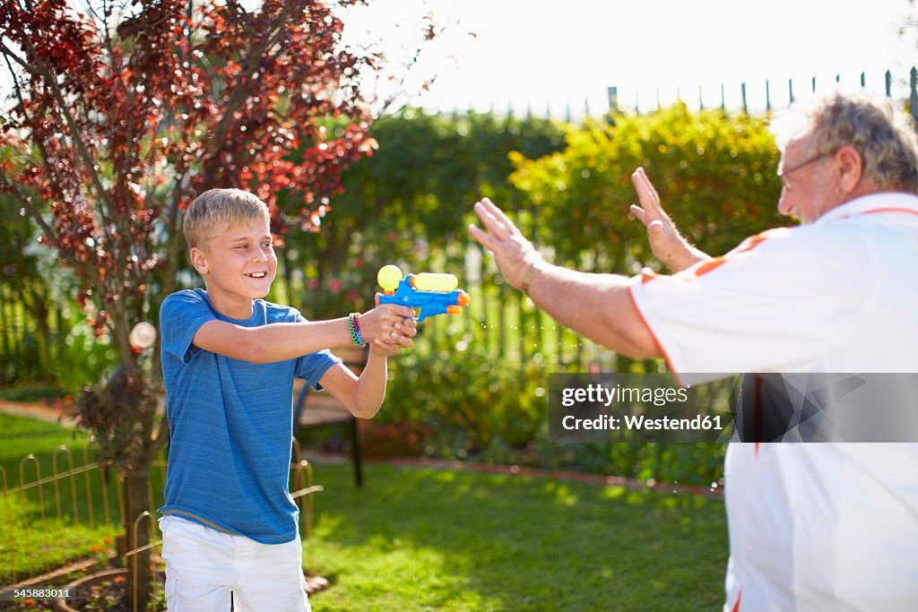 Grandson splashing at grandfather with water gun