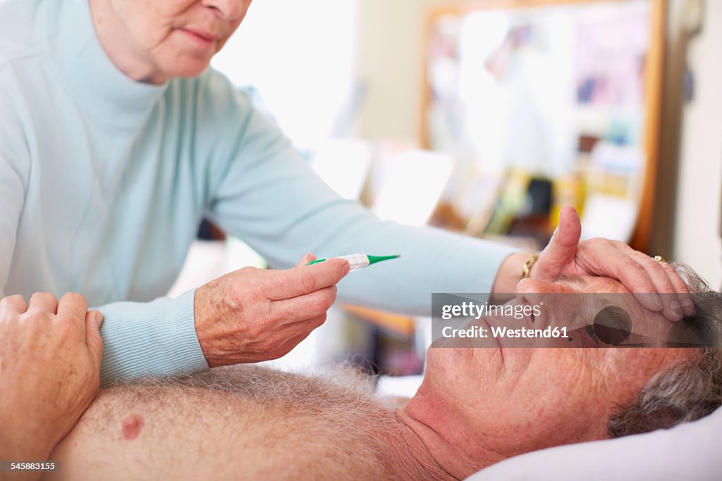 Senior woman taking temperature of sick husband at home