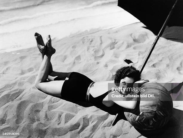 Joan Crawford *23.03..1977+Schauspielerin, USA- posiert in einem Badeanzug am Strand unter einem Sonnenschirm, ihren Kopf hat sie auf einem...