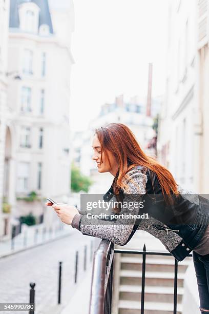 cheerful young woman leaning on railing and typing - balustrade stock pictures, royalty-free photos & images