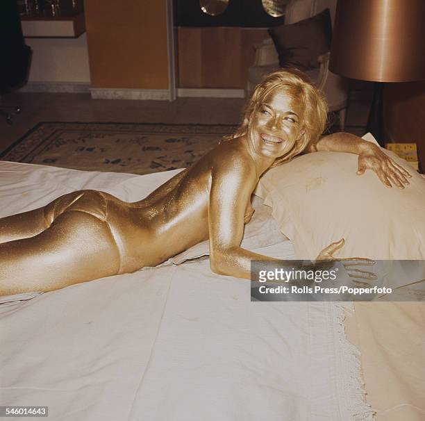 English actress Shirley Eaton, who plays the character of Jill Masterson, pictured covered from head to toe in gold paint by a painter on the set of...