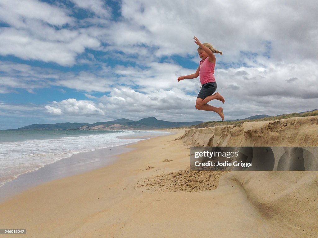 Girl jumping into the air off sand bank at beach