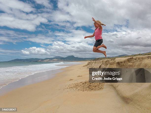 girl jumping into the air off sand bank at beach - jumping australia stock pictures, royalty-free photos & images