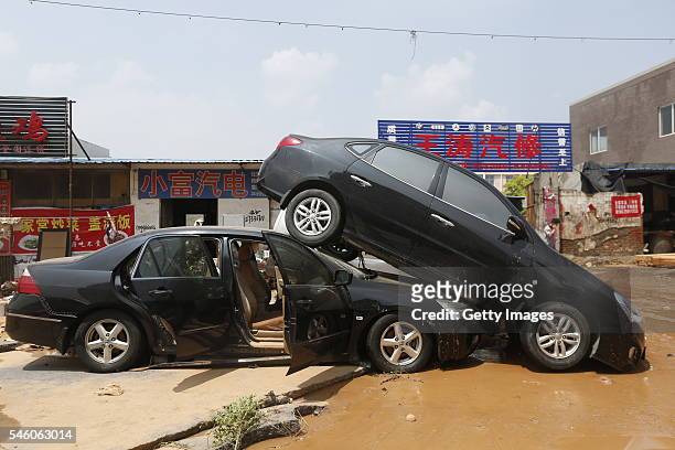 Man walks past two vehicles damaged by floodwaters on July 10, 2016 in Xinxiang, China. An overnight rainstorm hit Xinxiang in central China's Henan...